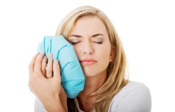 Young woman with dental pain pressing a bag of ice to her jaw.