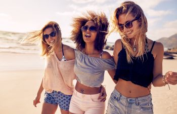 Three young women with perfect smiles enjouying a walk along a beach.