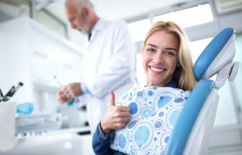 Happy woman in a dental chair after a checkup showing her thumb up.